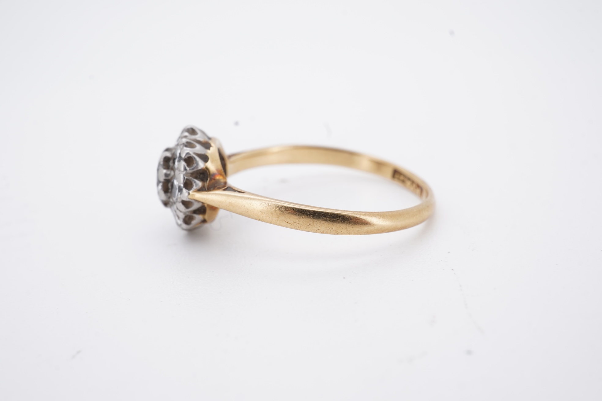 An early 20th century 18ct, plat. and nine stone diamond cluster ring, the central diamond weighing approximately 0.30ct, size Q, gross weight 3.1 grams.